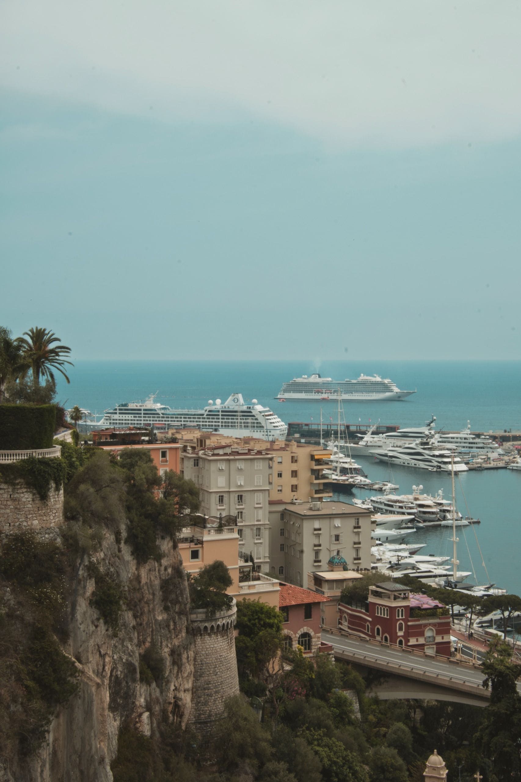 Vue sur le port avec des paquebots de croisière, des yachts et des bâtiments à flanc de falaise, au bord d'une mer turquoise sous un ciel voilé