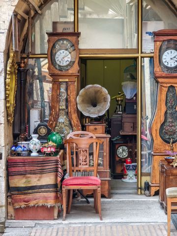 Entrée d'un magasin d'antiquités avec des horloges anciennes, un gramophone, des chaises et des objets décoratifs colorés