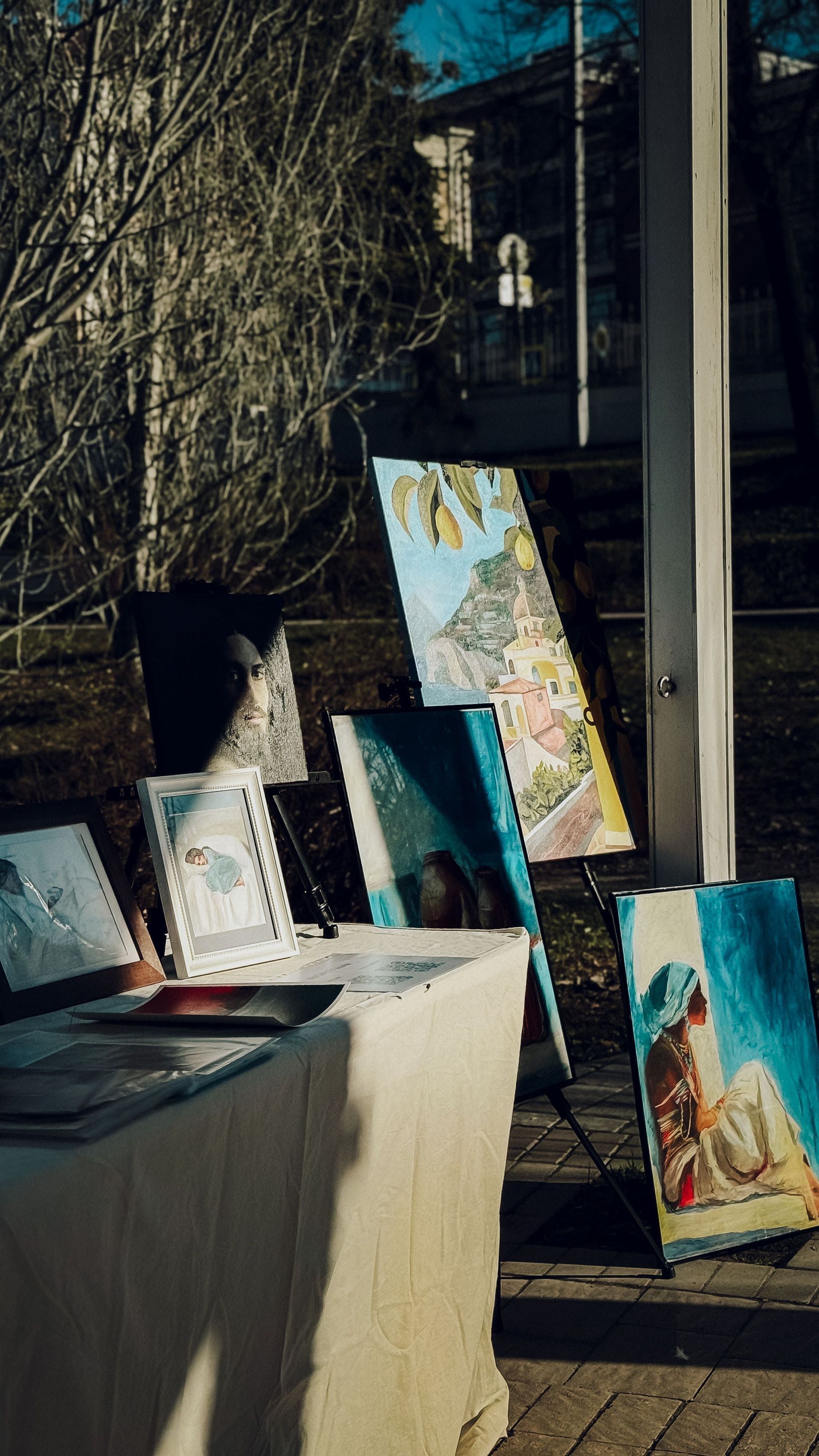 Exposition d'art en plein air avec des toiles colorées appuyées sur une table au soleil