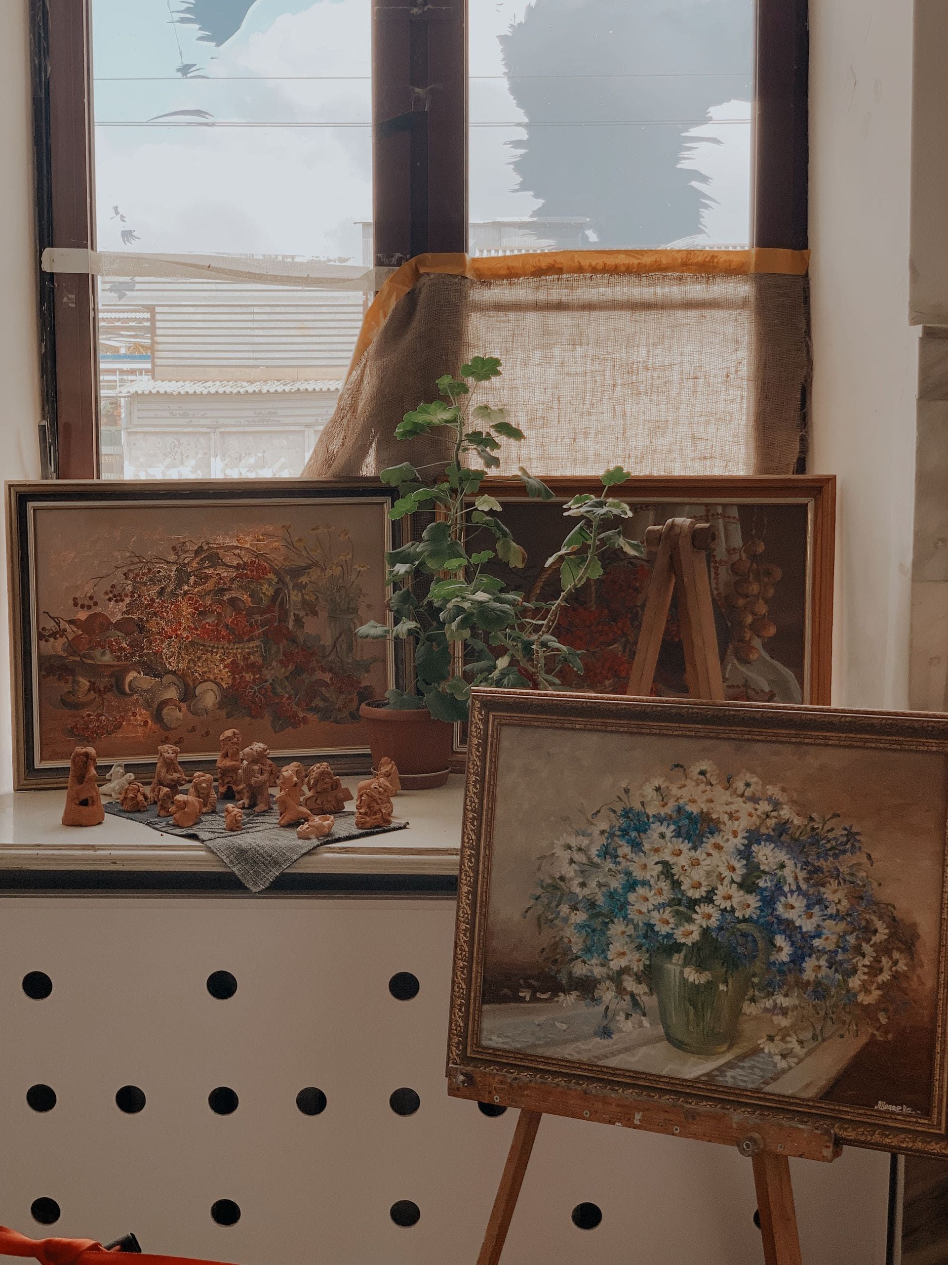 Des tableaux floraux encadrés sont exposés sur une étagère près d'une fenêtre, avec une petite plante en pot.