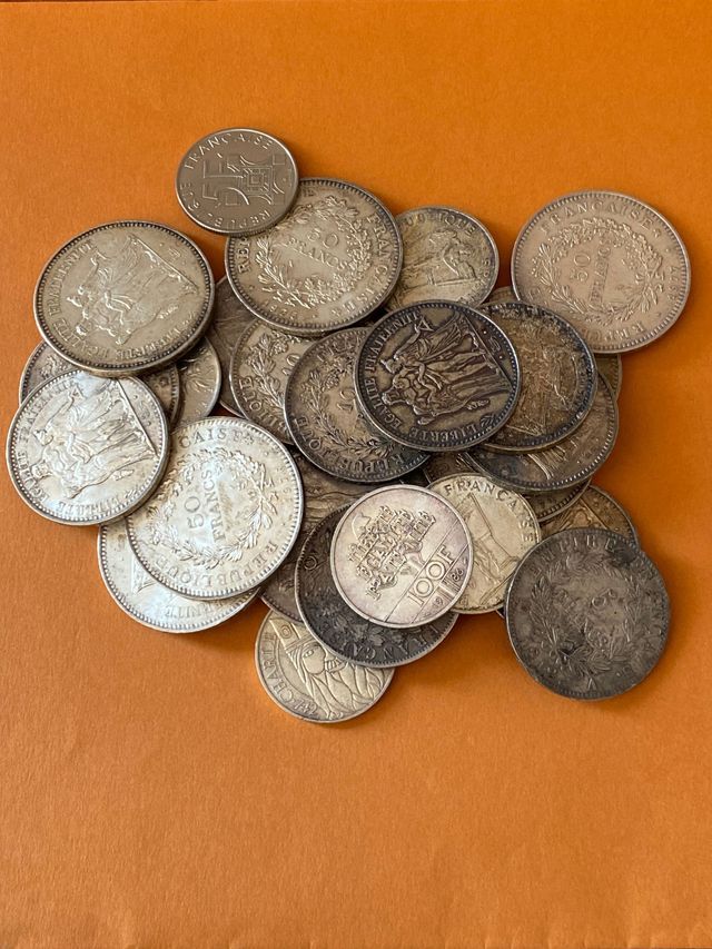 Un tas de pièces d'argent usées et de pièces sombres sur un fond orange