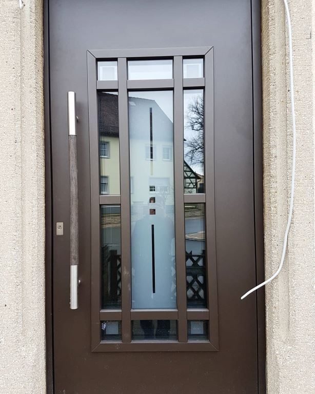 Braune Haustür mit rechteckiger Glasplatte, langem Griff und braunem Rahmen.