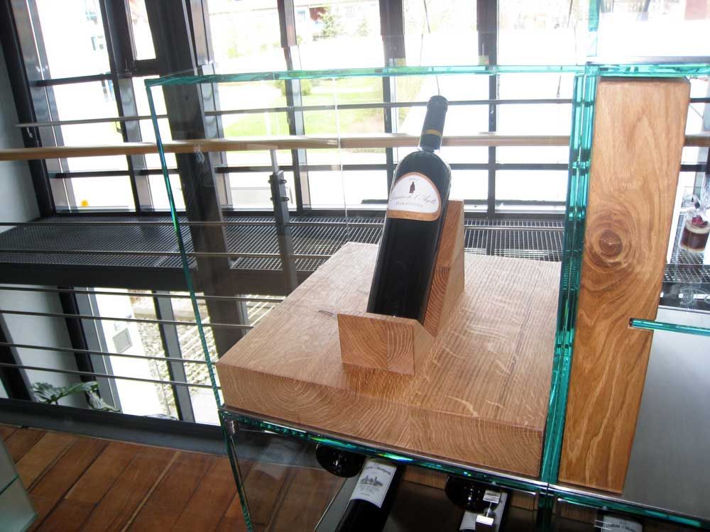 Eine Flasche Rotwein in einer Holzvitrine auf einem Glasregal.