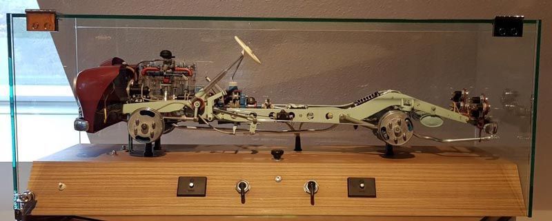 Ein Ausstellungsstück eines Oldtimer-Chassis, ausgestellt in einer Glasvitrine mit Holzsockel.