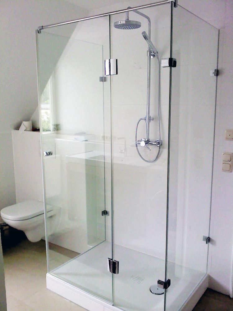 Glasduschkabine mit Chromarmaturen in einem weißen Badezimmer.