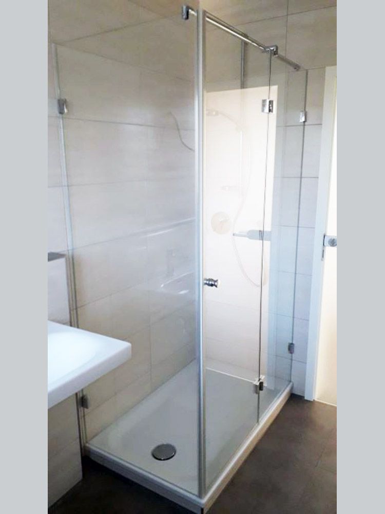 Glasduschkabine mit weißem Boden und gefliesten Wänden.