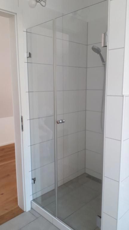 Glasduschkabine mit weiß gefliesten Wänden und grauem Duschboden.