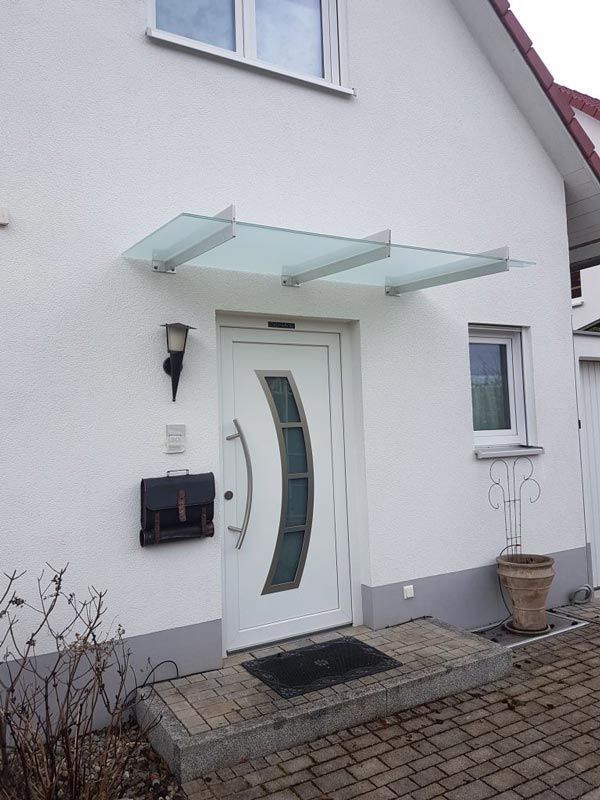 Weißer Hauseingang mit Glasmarkise, weißer Tür, schwarzem Briefkasten und kleinem Steinabsatz.