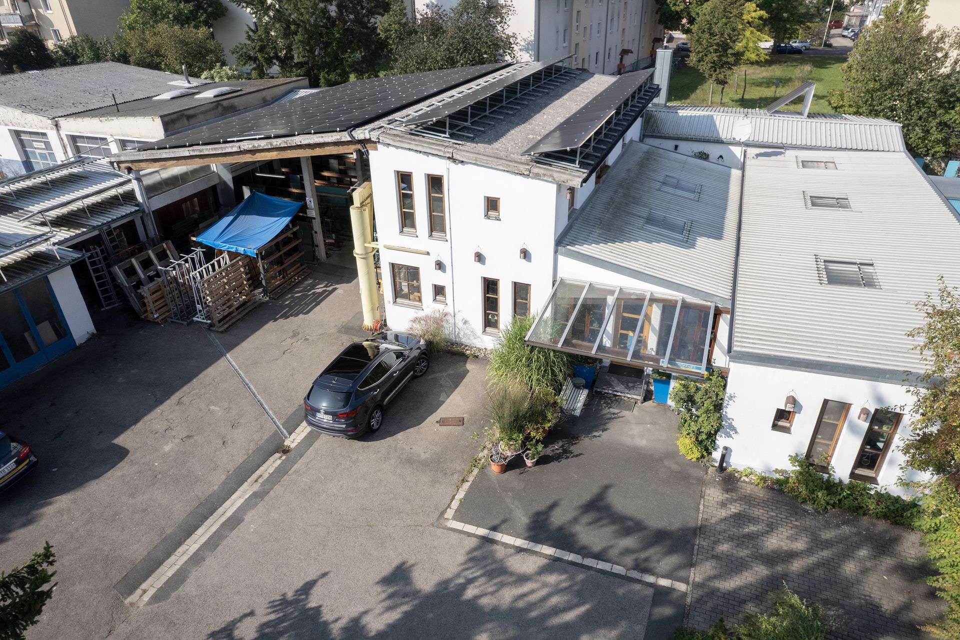 Luftbild eines weißen Gebäudes mit Solarmodulen. Davor ist ein schwarzes Auto geparkt.