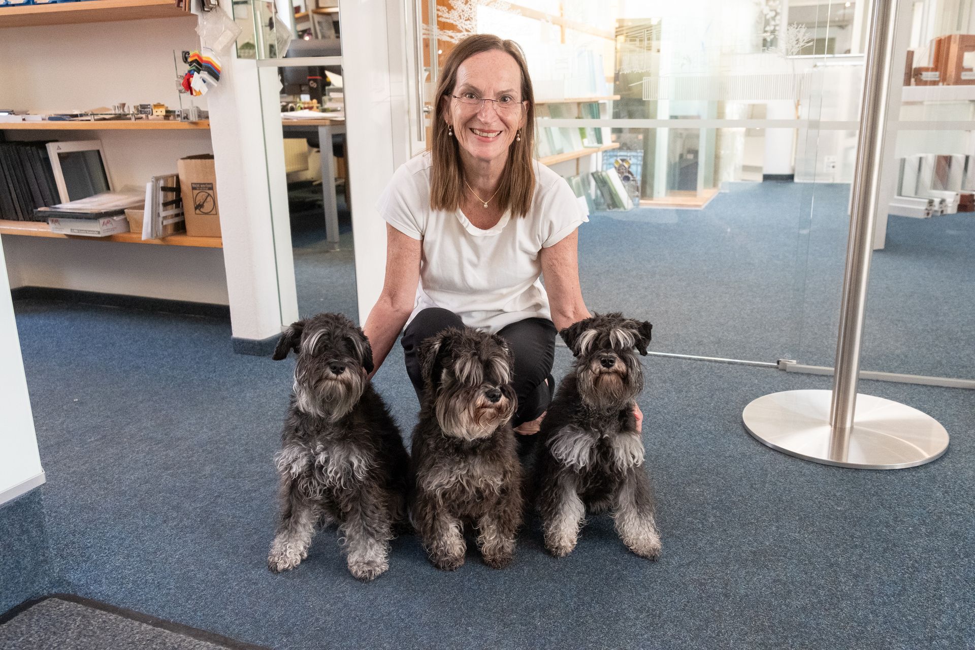 Frau mit Brille und drei Zwergschnauzerhunden sitzen auf einem blauen Teppich.