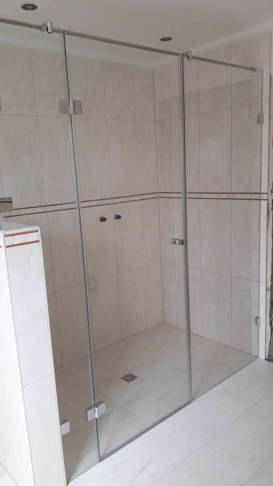 Glasduschkabine mit Chrombeschlägen in einem gefliesten Badezimmer.