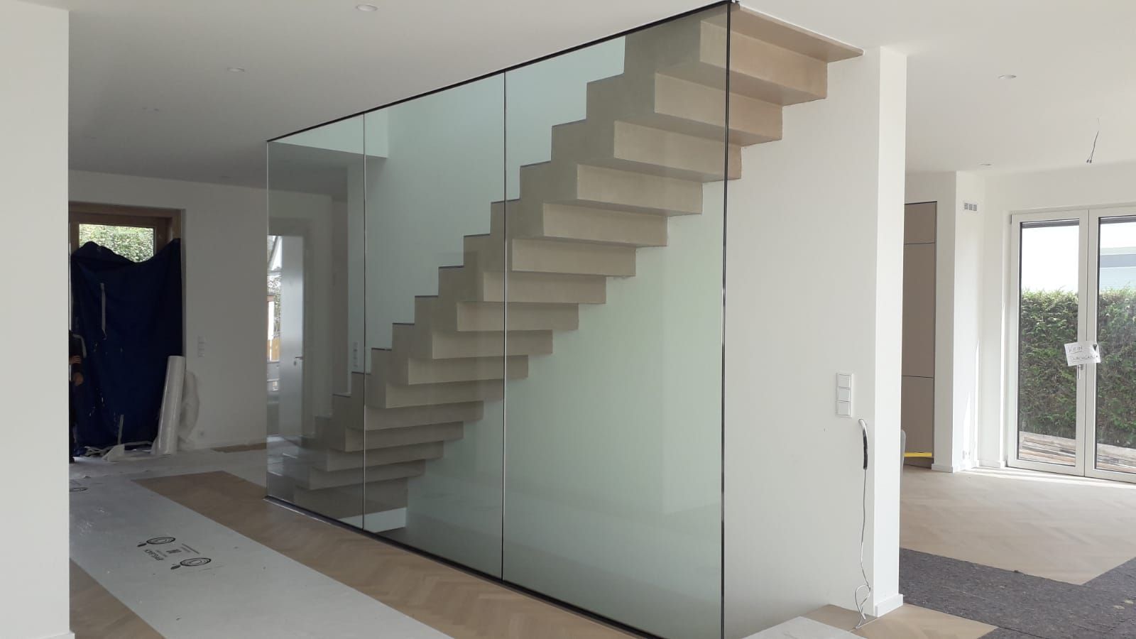 Treppe mit Glaspaneelen, beigen Stufen, weißen Wänden und Flur.