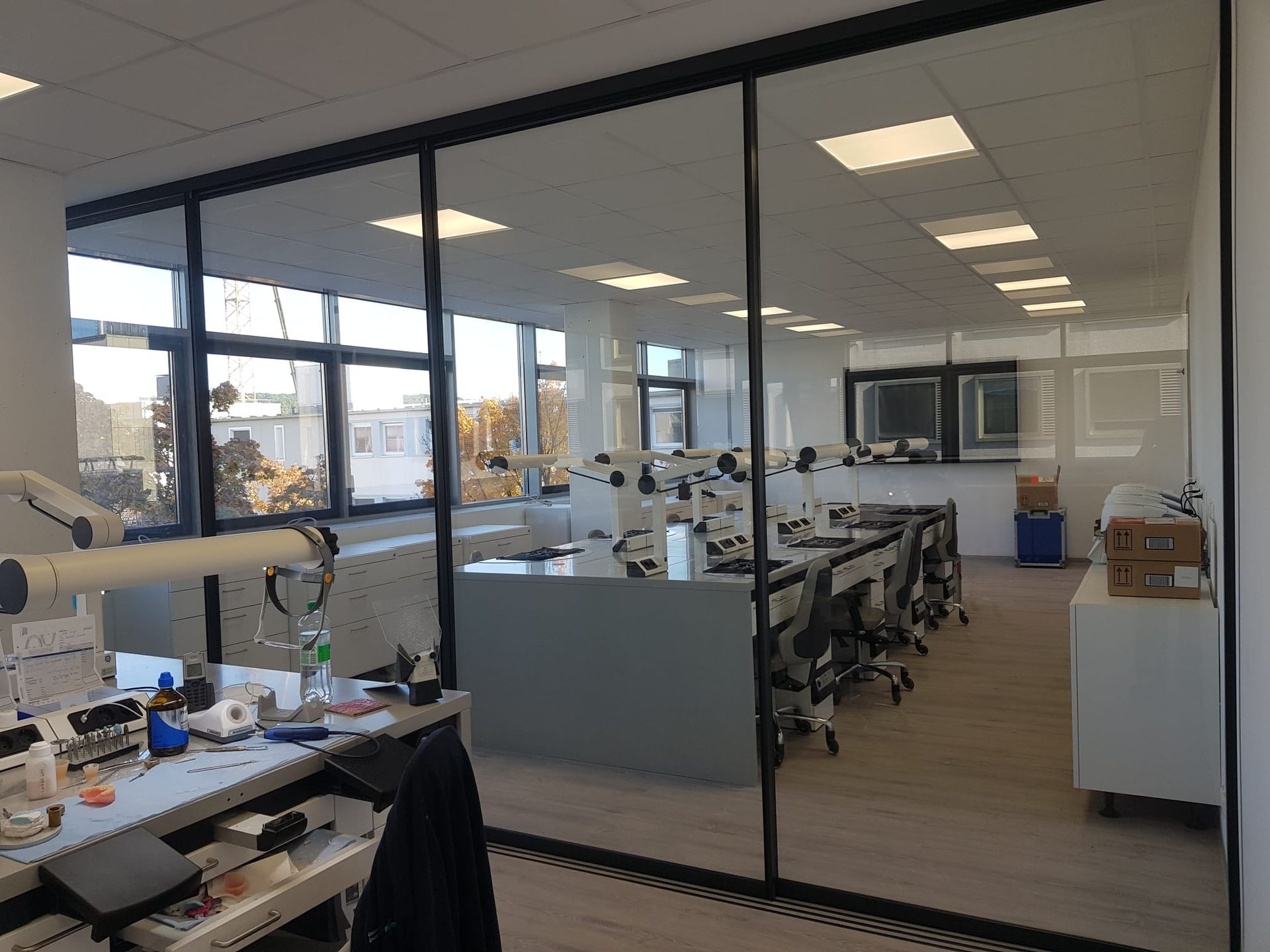 Büroräume mit Glaswänden, Schreibtischen, Stühlen und Tageslicht.