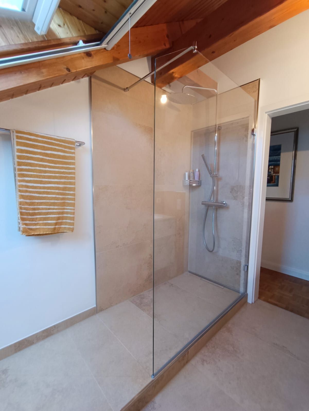 Modernes Badezimmer mit einer Duschkabine aus Glas, beigen Fliesen und einem Handtuchhalter.