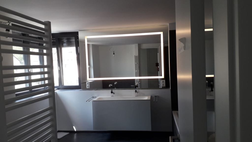 Modernes Badezimmer mit beleuchtetem Spiegel, Doppelwaschbecken und weißem Heizkörper.