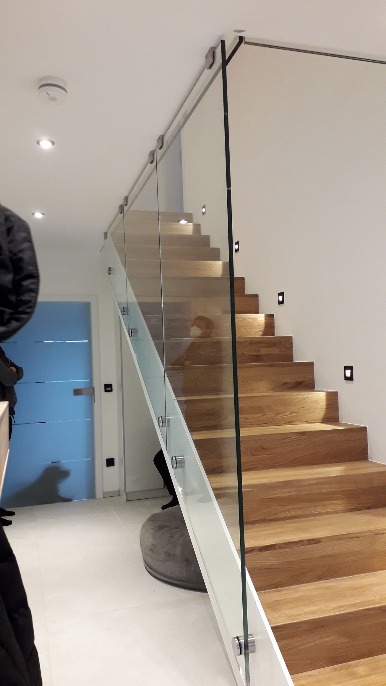 Treppe mit Glasgeländer, Holzstufen und stimmungsvoller Beleuchtung. Inneneinrichtung mit blauer Tür.