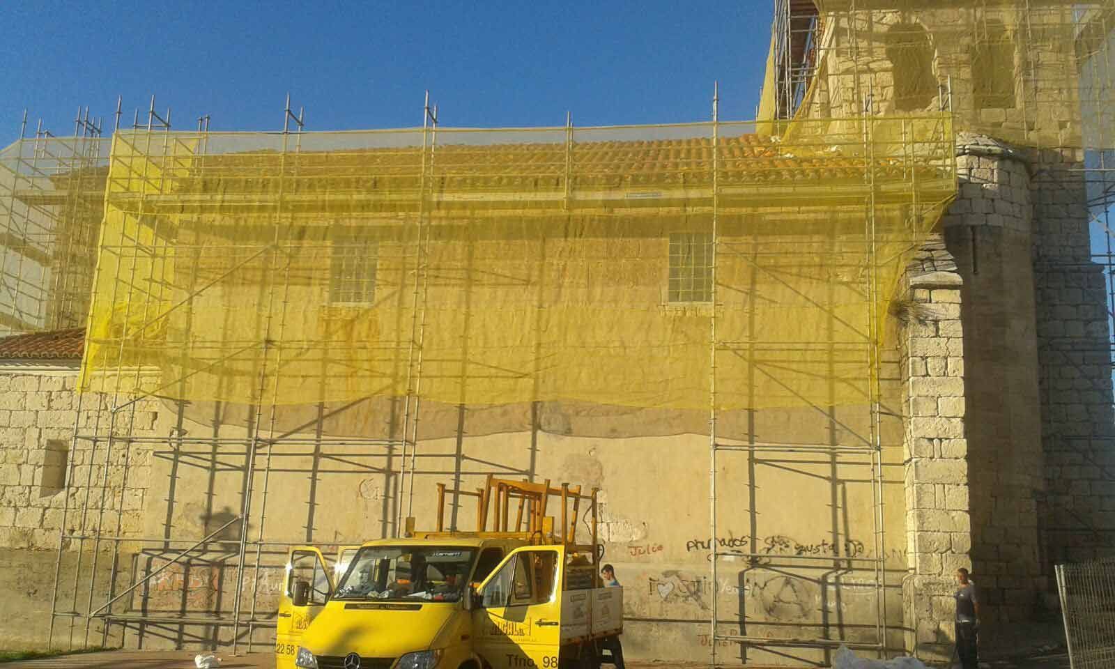 Un camión amarillo está estacionado frente a un edificio cubierto de andamios.