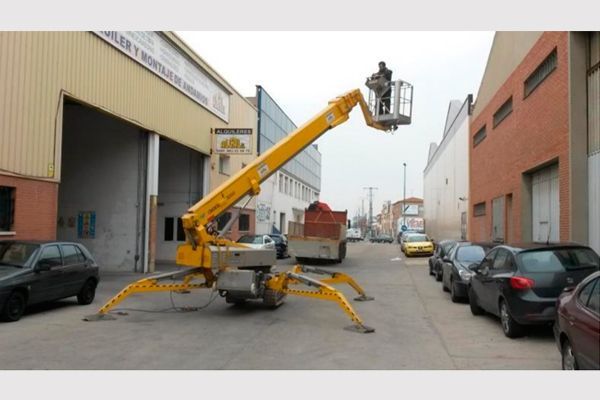 Un hombre está en un cubo sobre una grúa frente a un edificio.