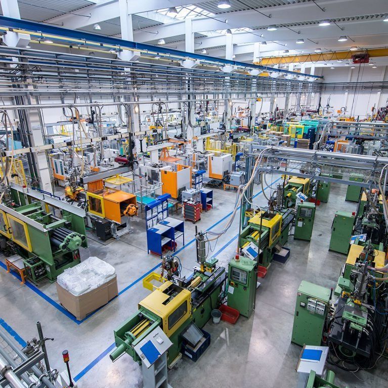 Große Industriehalle mit automatisierten Maschinen, Förderbändern, Rohrleitungen und orange-grünen Anlagen an der Decke.