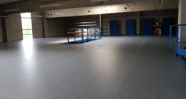 Leerer Innenraum mit grauem Boden, blauen Geländern und Türen an der Rückwand.