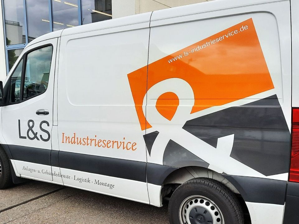 Weißer Servicewagen mit orange-schwarzem L&S Industriservice-Logo parkt vor einem Gebäude