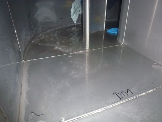 Innenraum eines leeren Metallschranks mit einem abgeplatzten Regalbrett und reflektierenden grauen Oberflächen