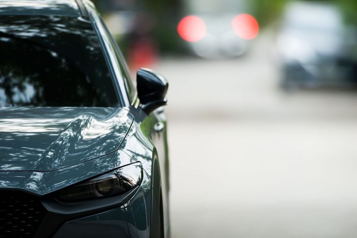 Parte delantera de un coche verde oscuro en una calle, con semáforos desenfocados al fondo