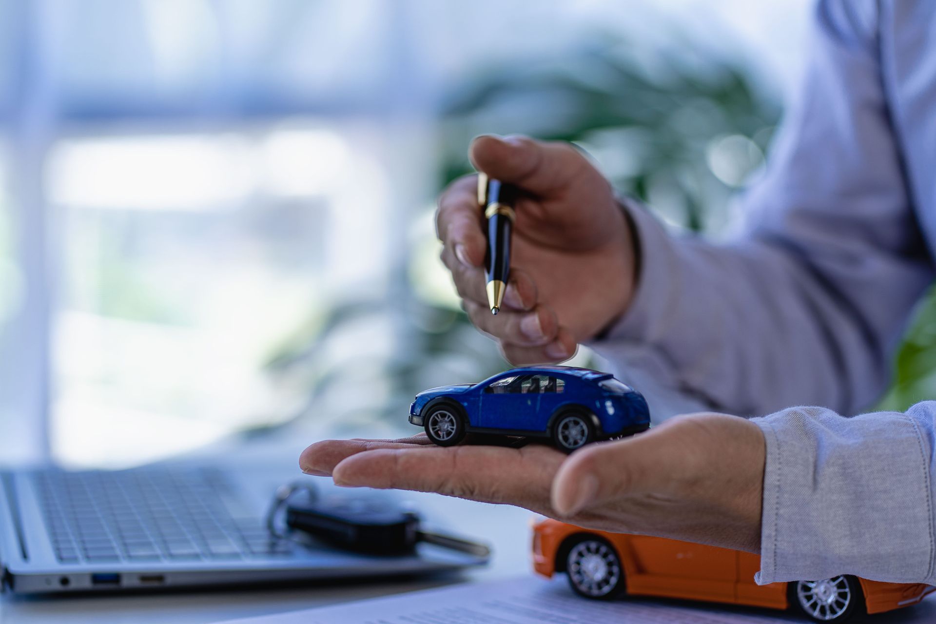 Una mano coloca un coche de juguete en el escritorio, junto a un portátil y una calculadora