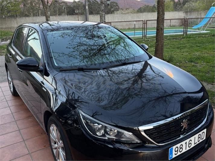 Sedán negro estacionado en una entrada mojada junto a un parque infantil, con reflejos de árboles en el capó