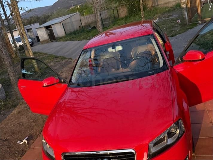 Coche rojo aparcado al aire libre, con las dos puertas delanteras abiertas en una entrada para vehículos.