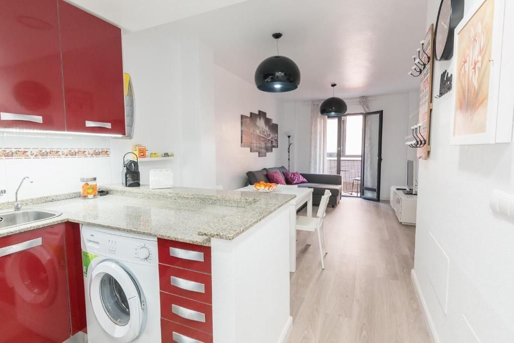 Cocina moderna y sala de estar con gabinetes rojos, lavadora y balcón.