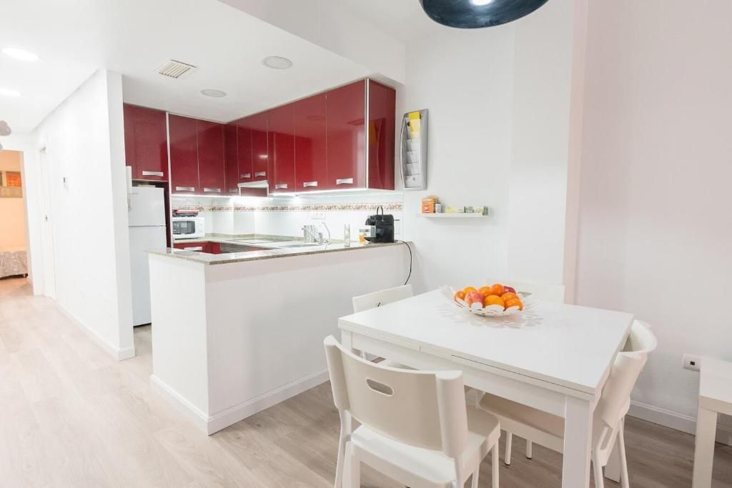 Cocina moderna con gabinetes rojos, isla blanca y mesa de comedor blanca.