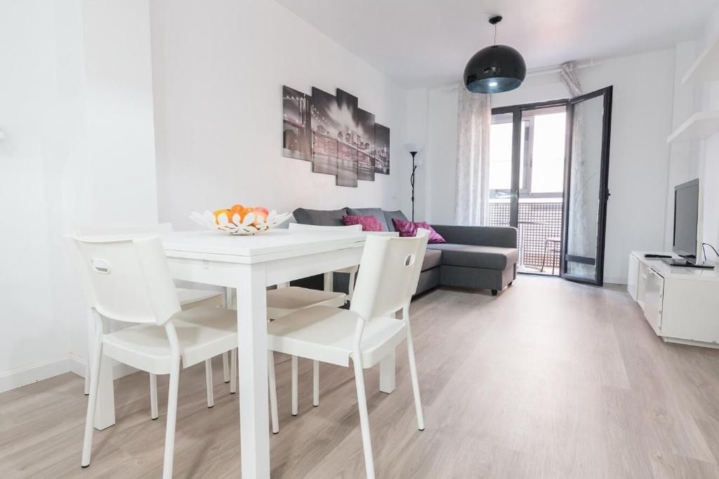 Sala de estar con mesa y sillas blancas, sofá gris, balcón y arte.