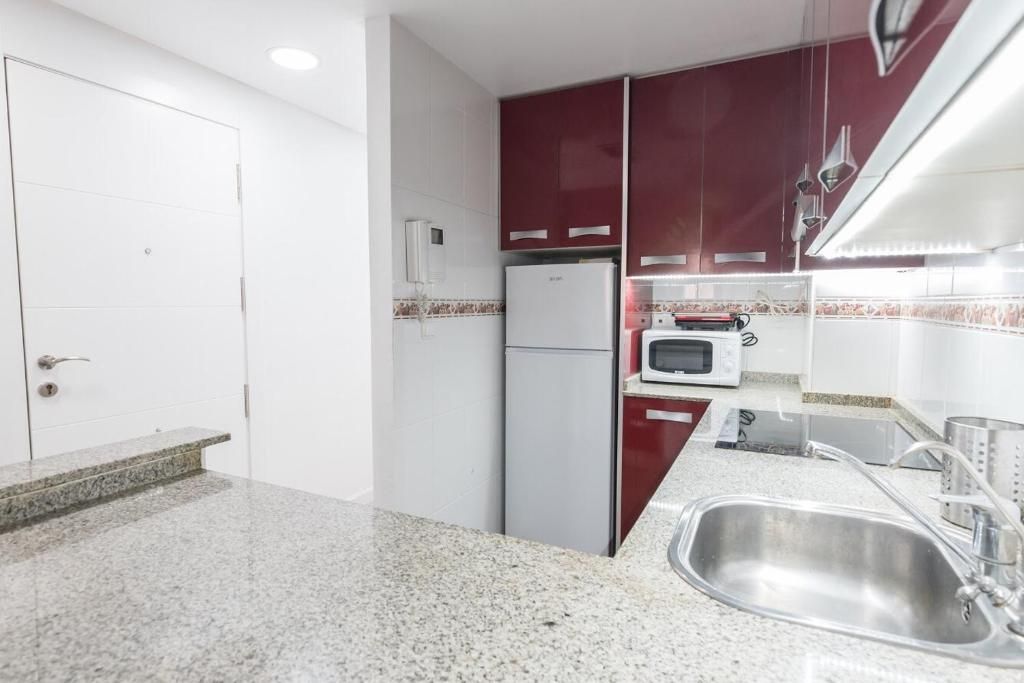 Cocina con gabinetes rojos, fregadero de acero inoxidable, refrigerador y microondas.