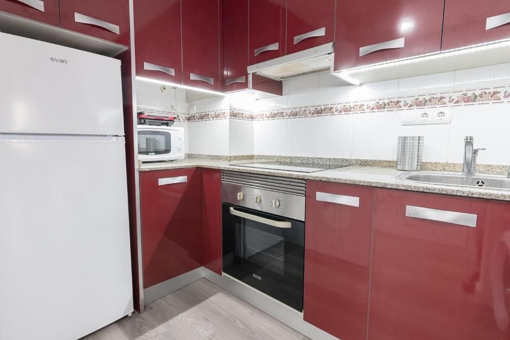 Cocina roja y blanca con refrigerador, gabinetes y estufa.