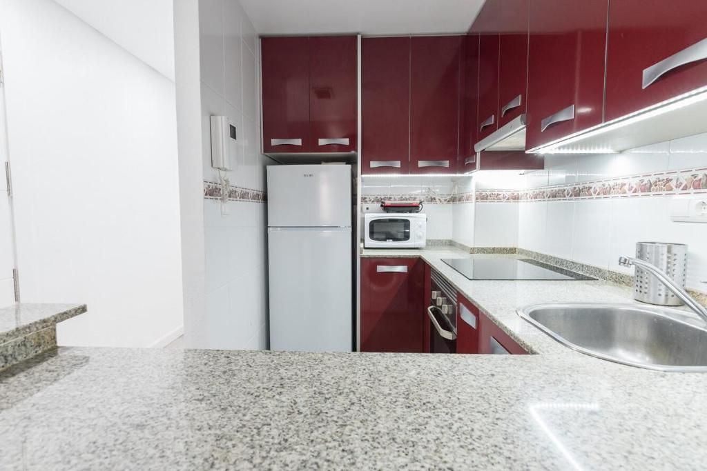 Cocina con gabinetes rojos, electrodomésticos blancos y encimera de granito.