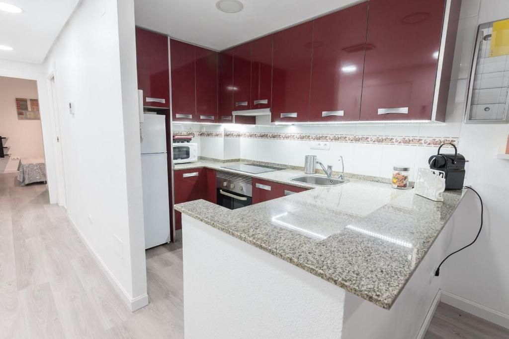 Cocina con gabinetes rojos, encimera de granito, electrodomésticos de acero inoxidable y entrada de pasillo.