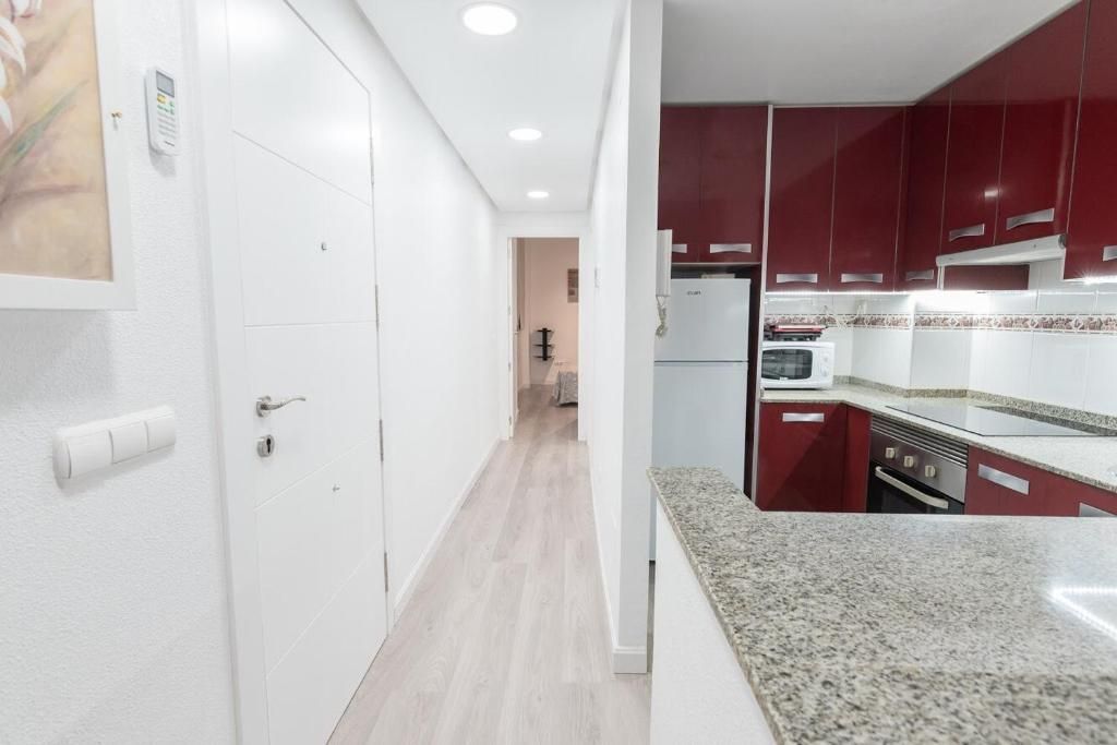 Pasillo que conduce a una cocina con gabinetes rojos y una encimera clara.