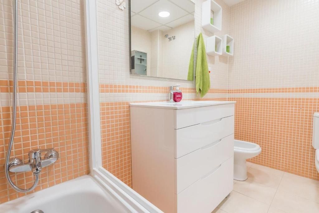 Baño con azulejos color durazno y blanco, tocador blanco y ducha/bañera.