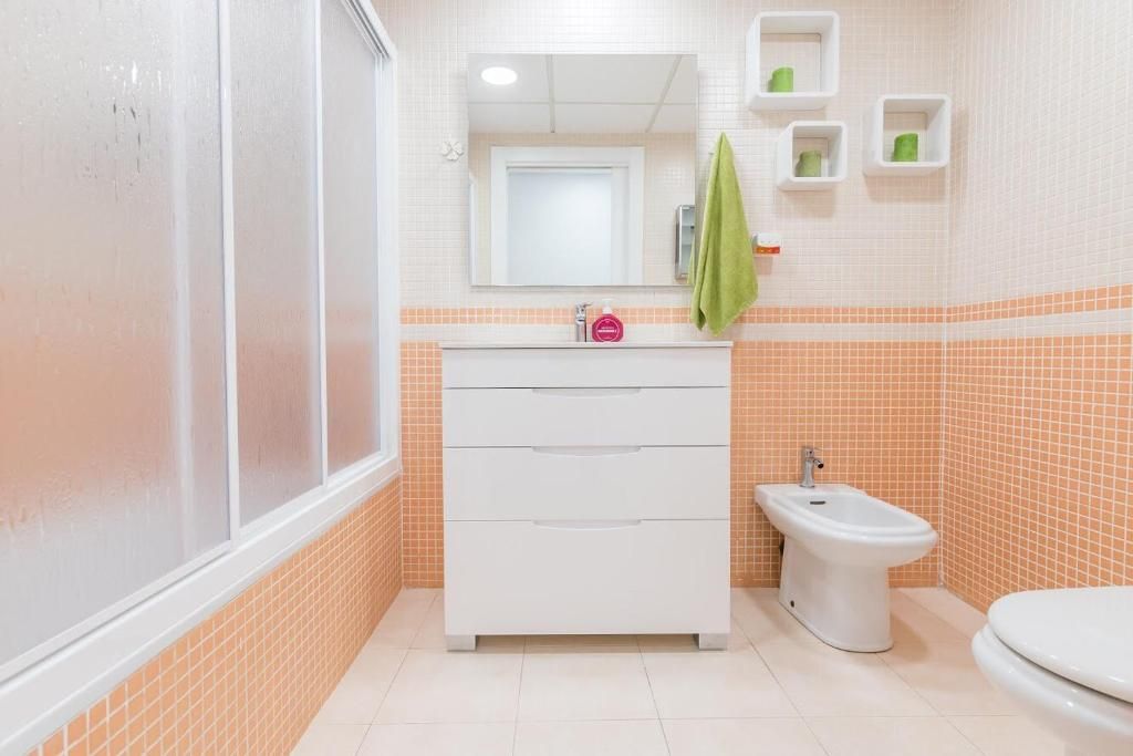 Baño con azulejos naranjas, tocador y sanitario blancos, ducha, espejo y toalla verde.