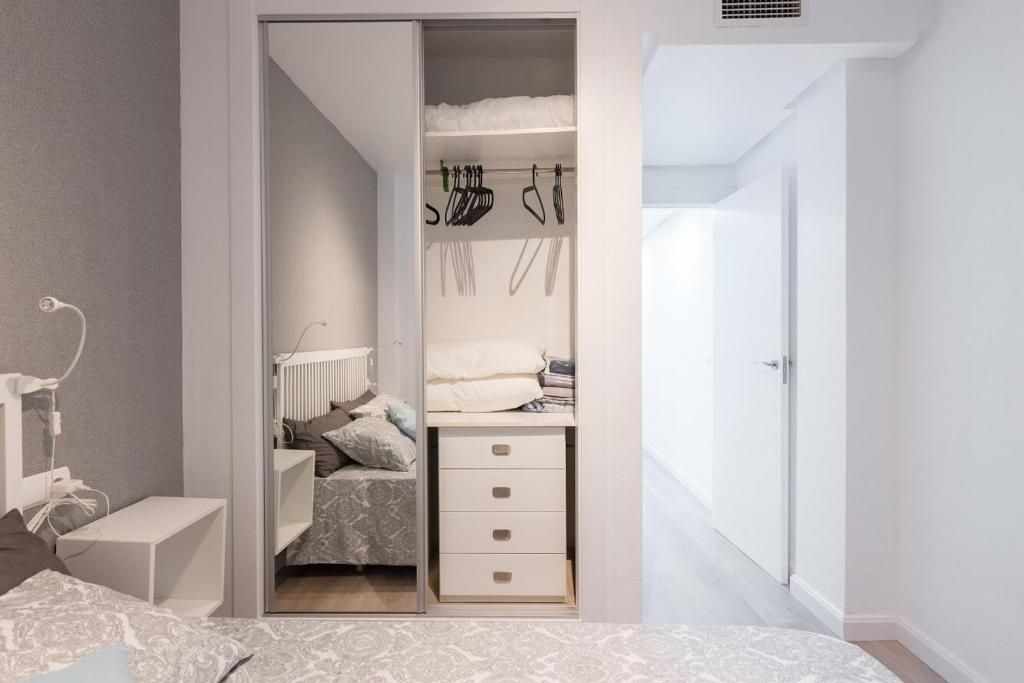 Dormitorio con armario con puerta corrediza con espejo abierta, mostrando ropa, cajones y cama con almohadas.