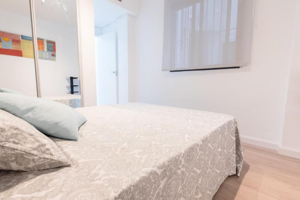 Dormitorio con una cama con ropa de cama estampada en gris y almohadas azul claro. Se ve una ventana con una cortina.