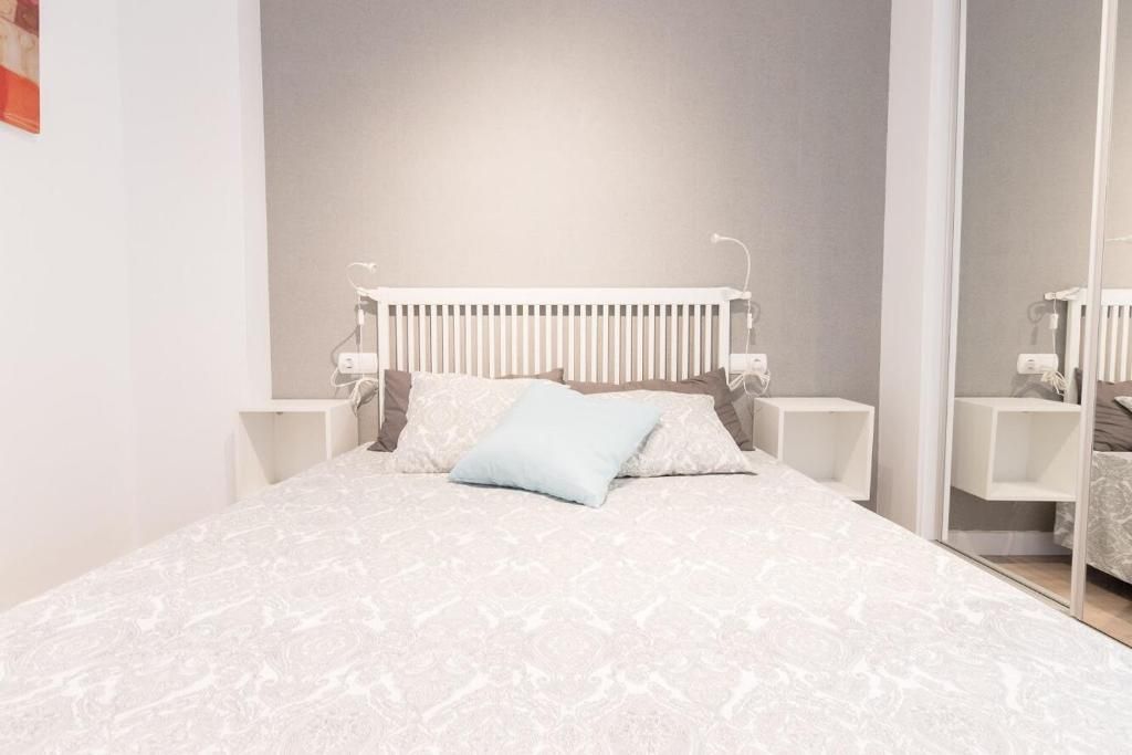 Dormitorio con cabecero blanco, pared gris, cama con funda estampada, mesitas de noche y espejo.