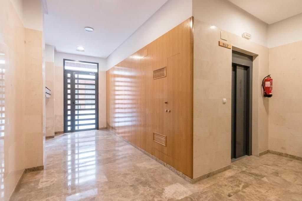 Pasillo con suelo de mármol, revestimiento de madera, ascensor y puerta de entrada.
