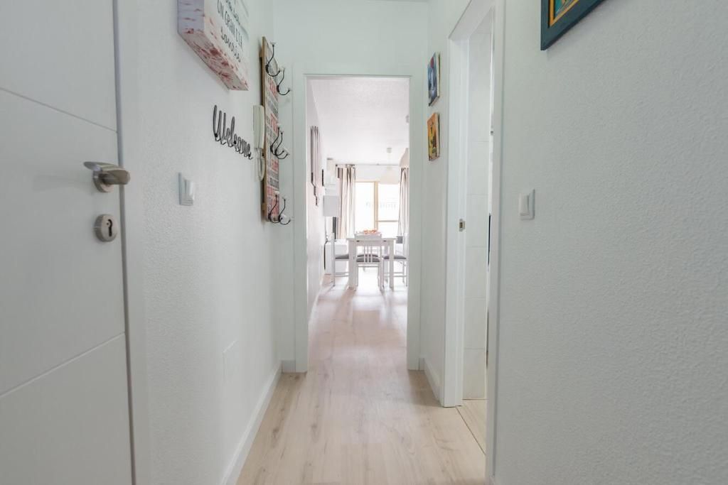 Pasillo largo y blanco que conduce al comedor. Suelo de madera clara, paredes y puertas blancas con decoración.