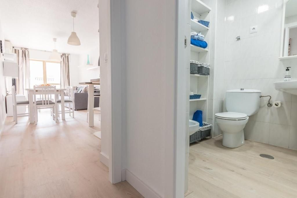 Un pasillo blanco y luminoso conduce al comedor a la izquierda y a un baño a la derecha con inodoro y estantes.