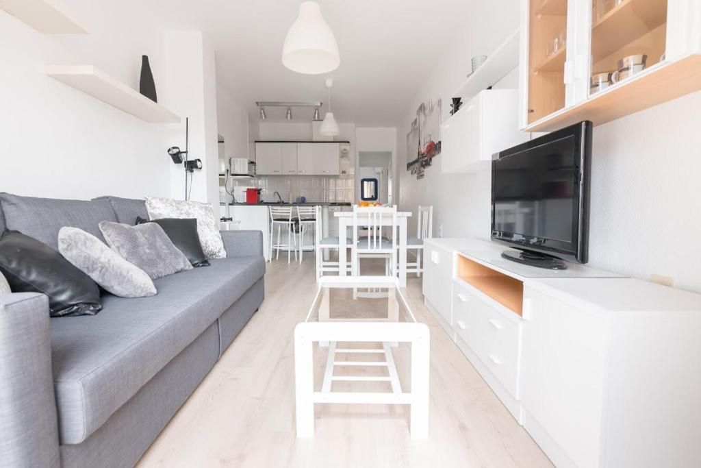 Sala de estar con sofá gris, muebles blancos y TV.