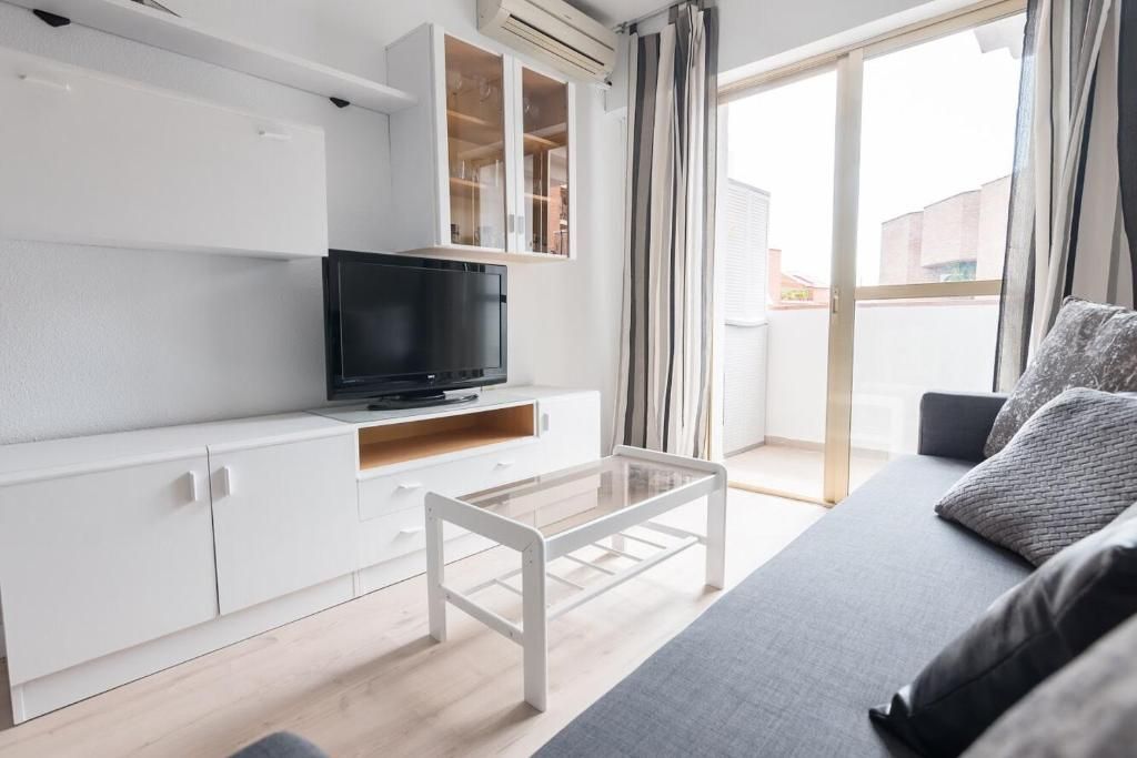 Sala de estar con muebles blancos, TV y acceso al balcón.