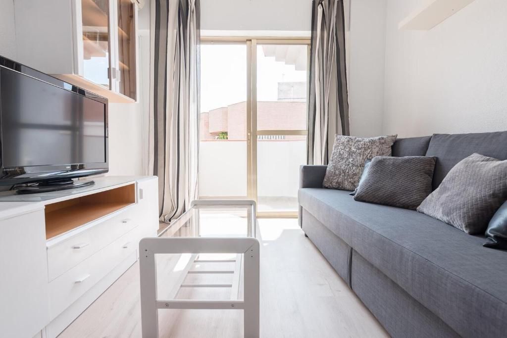 Sala de estar con sofá, TV y puerta de balcón abierta; combinación de colores gris y blanco.