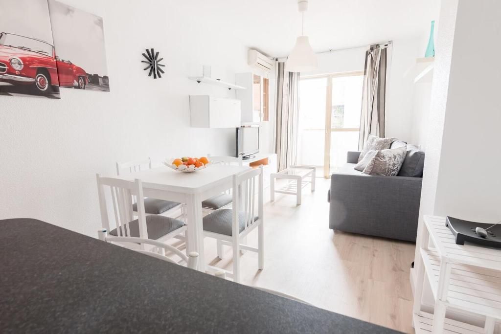 Sala de estar con paredes blancas, mesa de comedor, sofá y acceso al balcón.